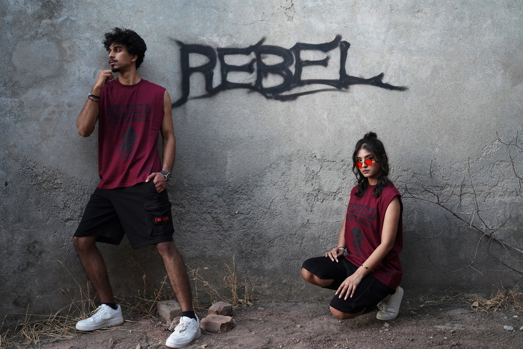 Two people in matching outfits against a wall with 'REBEL' graffiti.