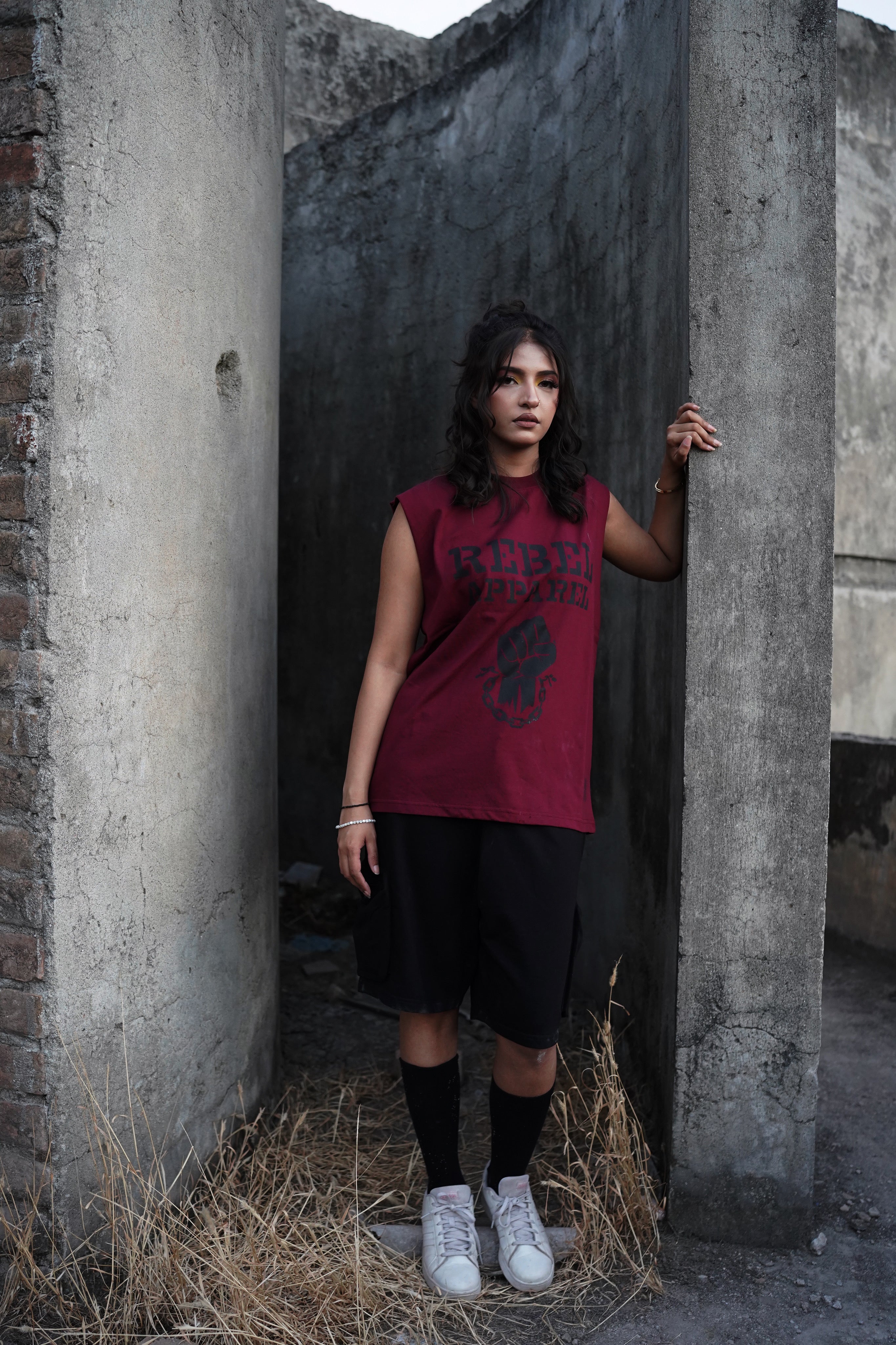 Woman in a red sleeveless top and black shorts standing in a dilapidated building.