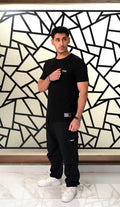Man wearing a black t-shirt and pants standing in front of a geometric patterned wall.