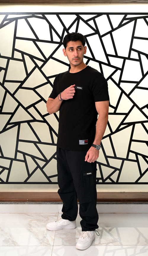 Man wearing a black t-shirt and pants standing in front of a geometric patterned wall.