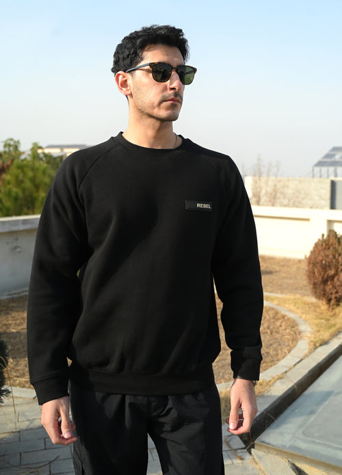 Man wearing a black sweatshirt with a logo, standing outdoors.